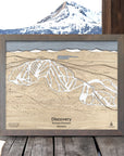 Wooden ski map of Discovery Ski Area with a lake, framed against a scenic background.
