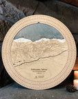 A 16" round wooden cribbage featuring an engraved detailed ski map of Palisades Tahoe ski resort, set against a rustic stone wall with lit candles and pinecones.