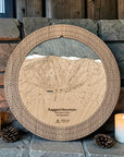 Ragged Mountain cribbage board in Weathered Timber beside a stone fireplace with candles and pinecones.