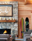 Large format framed map of Ski Butternut Ski Resort above a fireplace in a luxurious ski cabin with vintage snowboards on display.