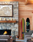 Living room with stone fireplace, large format solitude ski map, gray sofa, and two snowboards against a wooden wall.