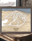 Framed laser-cut map of Terry Peak ski trails in South Dakota on a wooden surface inside a rustic ski cabin.