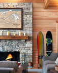 Large format artwork of Yellowstone Club Ski Resort in a luxurious ski house with fireplace, sofas, and vintage snowboards.