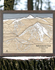 Layered, wooden map of Yellowstone Club Ski Trails on a tree stump with a forest background. Torched Peaks artwork designed by Shawn Orecchio