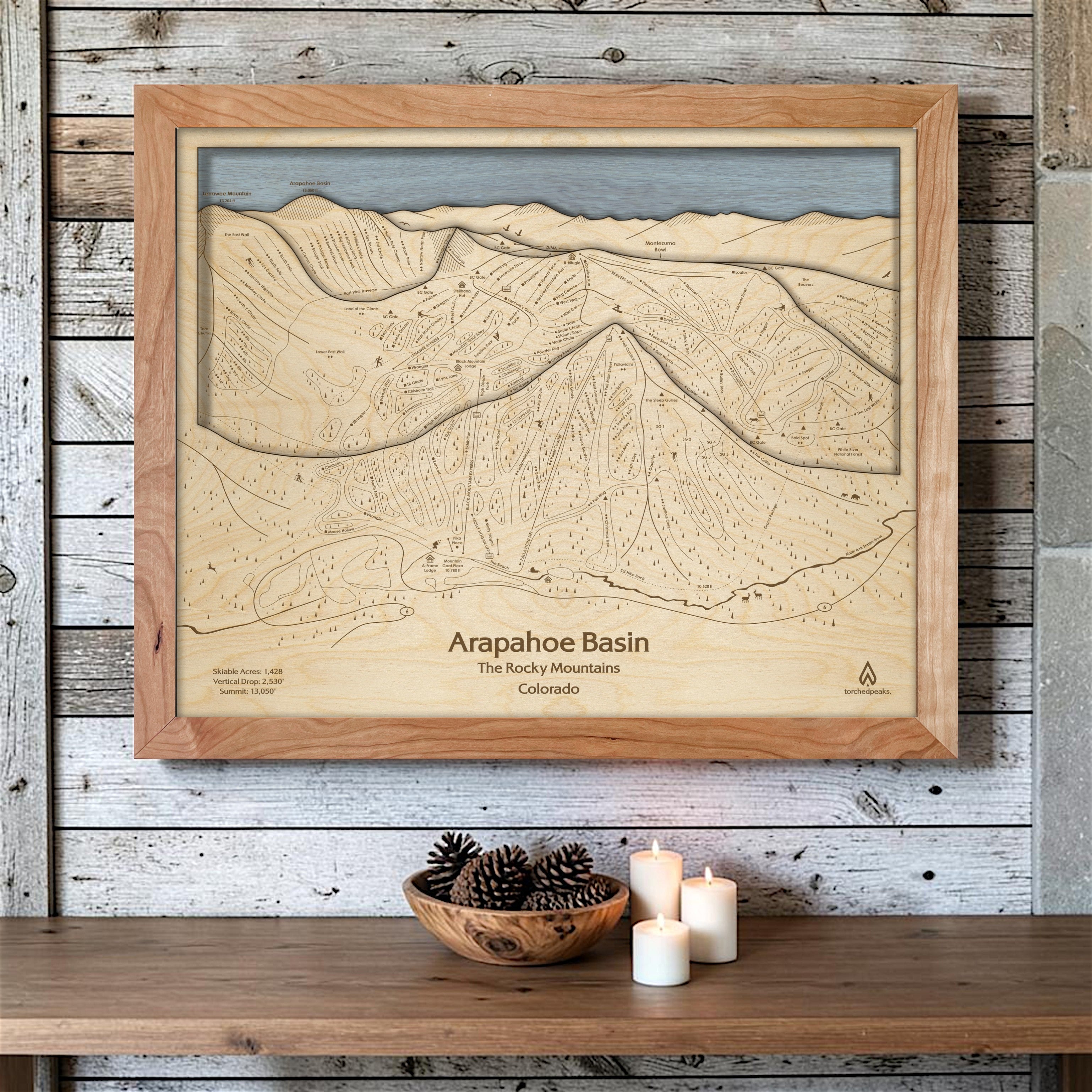 Natural Arapahoe Basin wooden ski map mounted on a whitewashed plank wall above candles and pinecones as ski cabin décor.