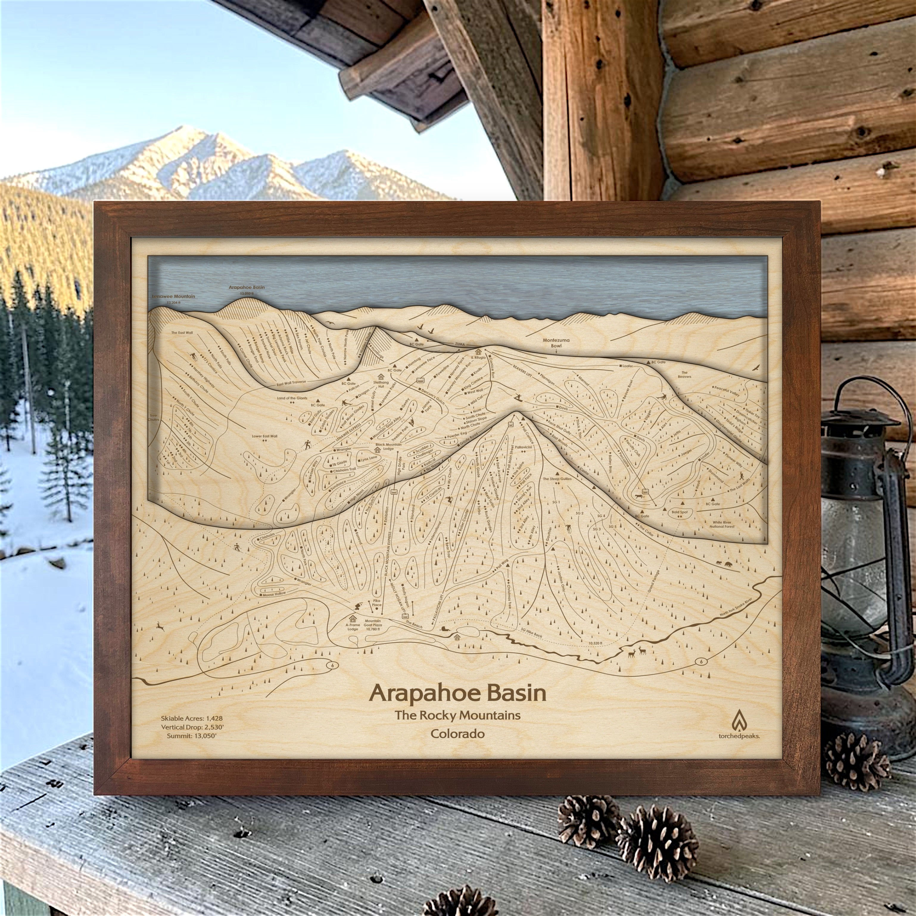 Rustic Mocha Arapahoe Basin framed ski map displayed on a cabin porch with snowy mountains in the background, a unique gift for skiers.
