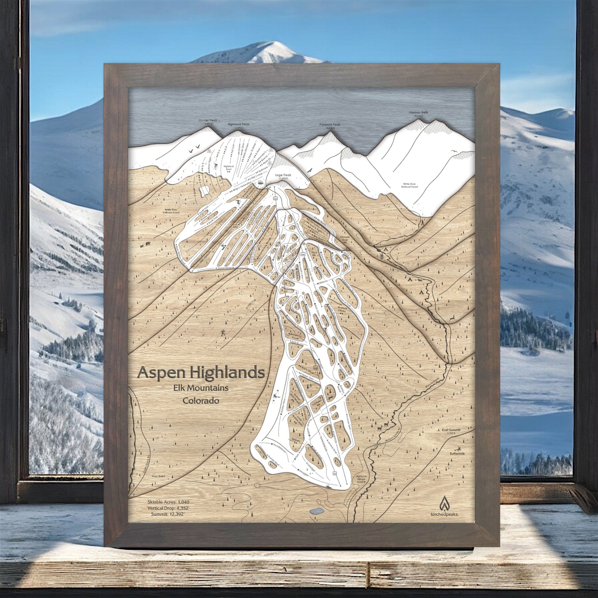 Wooden map of Aspen Highlands ski area with a mountain view in the background