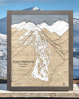Wooden map of Aspen Highlands ski area with a mountain view in the background