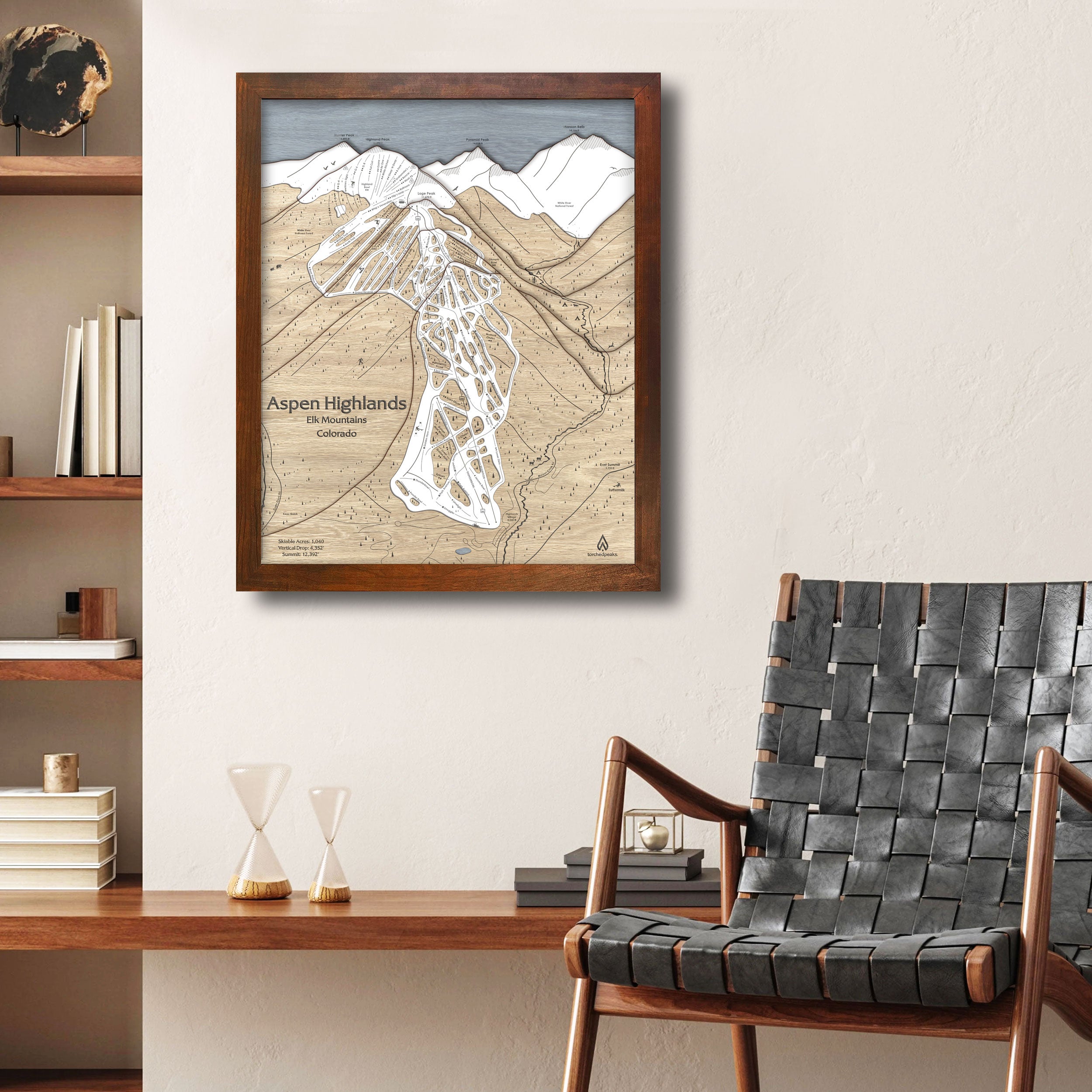 Framed map of Aspen Highlands on a wall above a wooden desk with a chair.