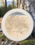 Arctic White Beaver Creek ski map cribbage board displayed outdoors against a pine tree in a mountain setting.
