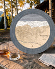 Graphite Grey Breckenridge ski map cribbage board on an outdoor cabin table beside whiskey glasses.