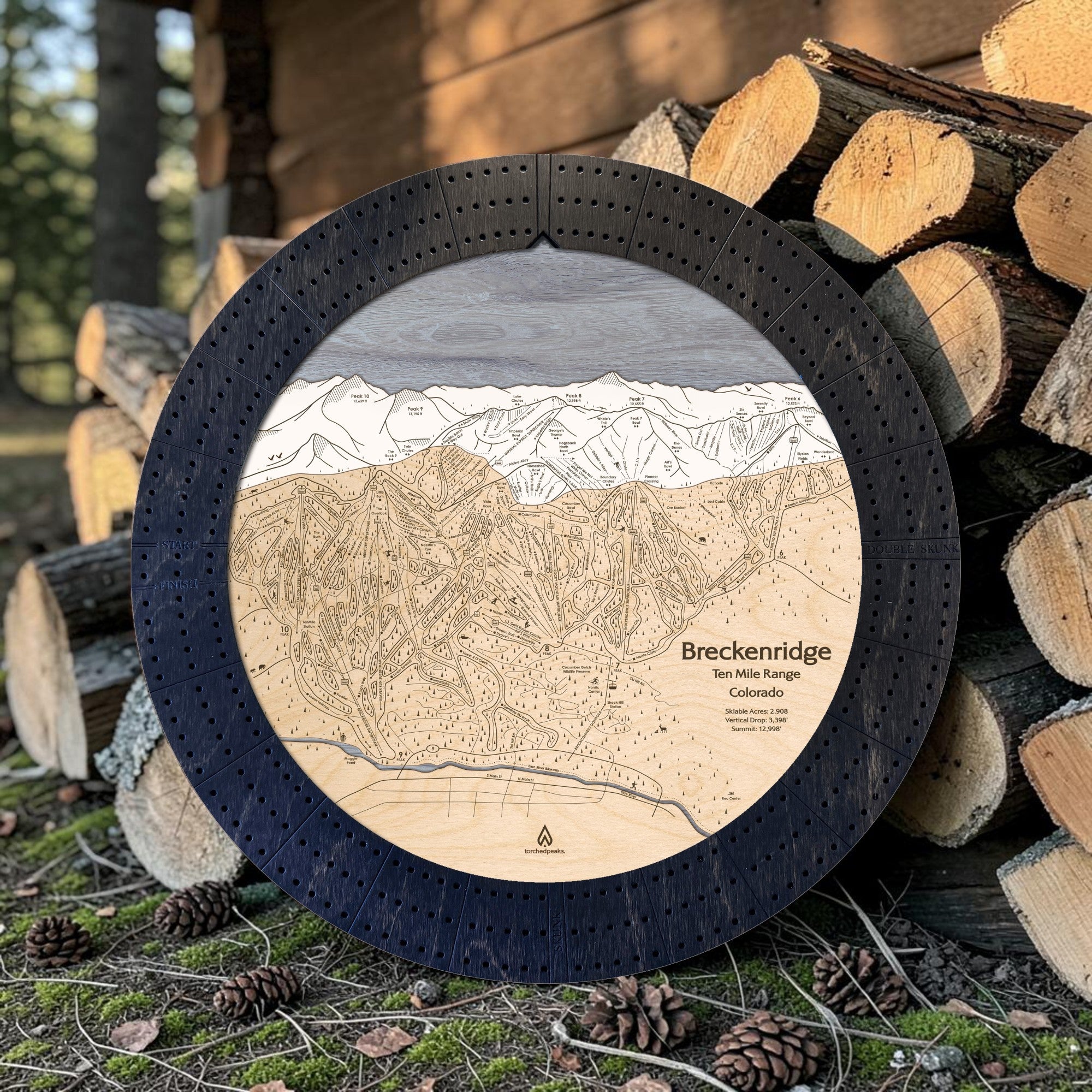 Matte Onyx Breckenridge ski trail map cribbage board displayed beside stacked firewood