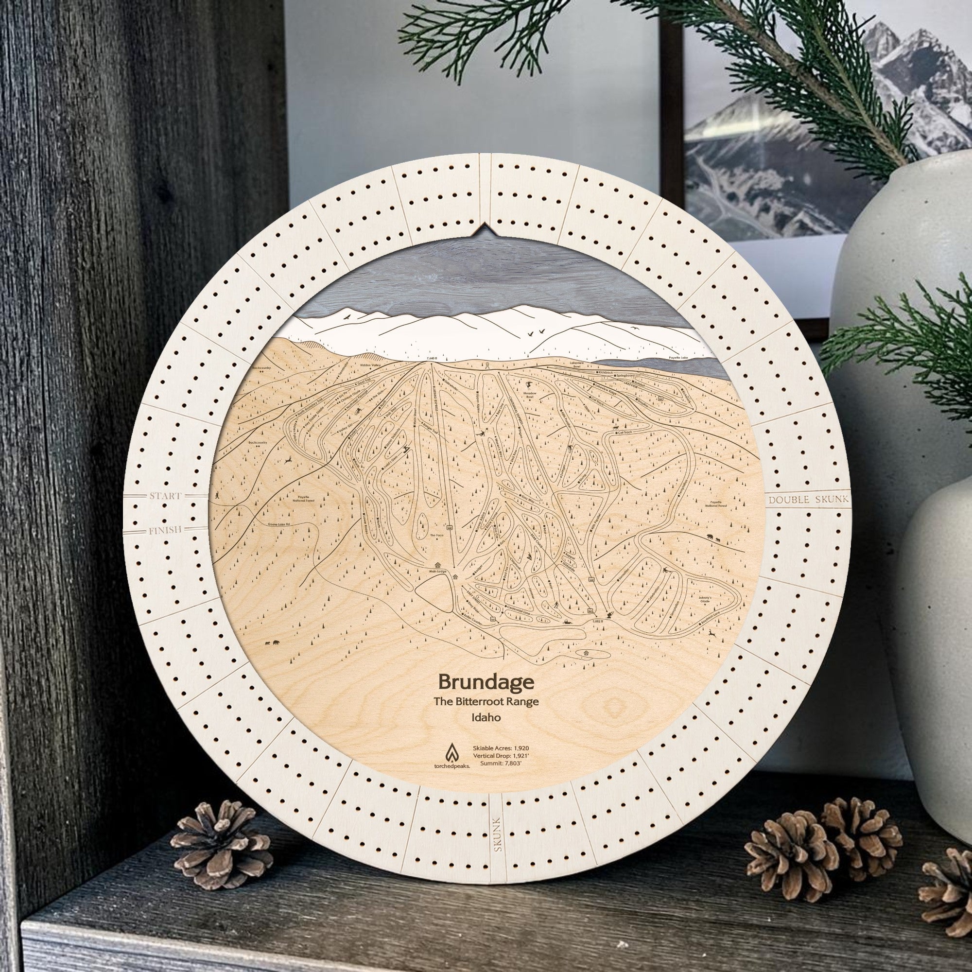 Arctic White Brundage Mountain ski map cribbage board displayed with pinecones and greenery as ski cabin décor.