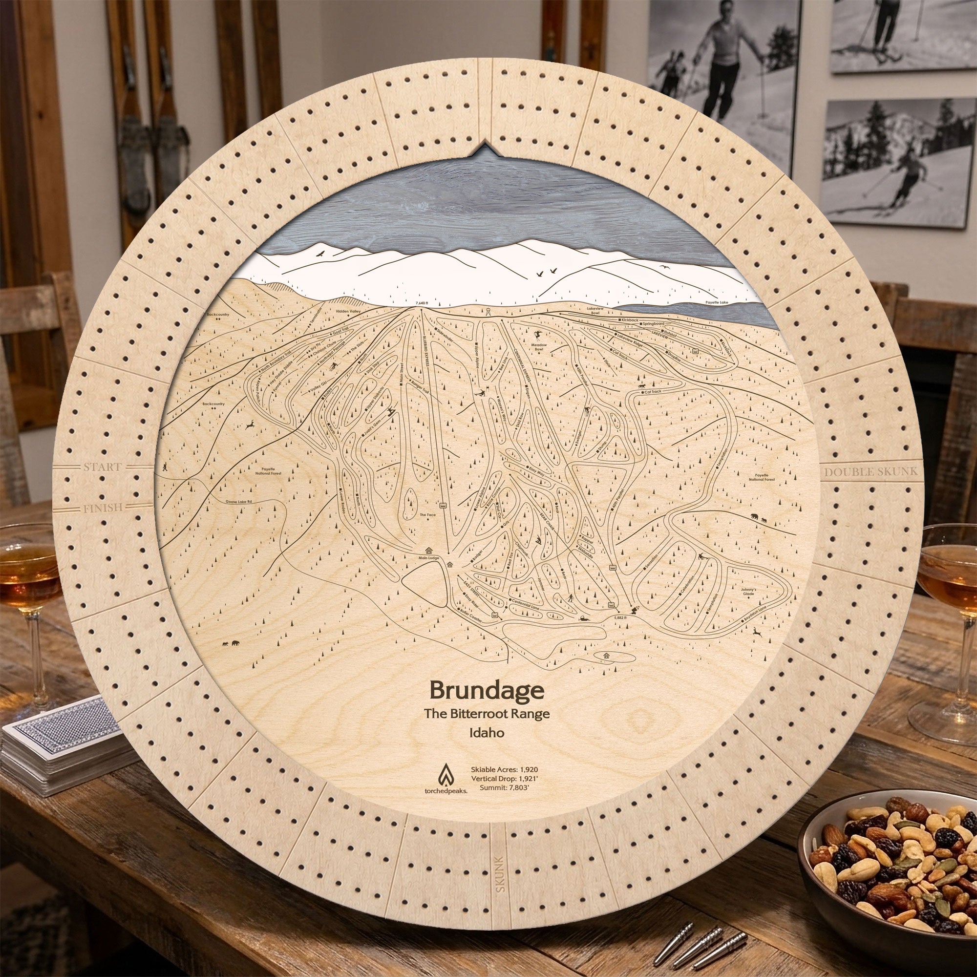 Birch Brundage Mountain ski trail map cribbage board displayed on a wooden table with playing cards and snacks.