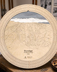 Birch Brundage Mountain ski trail map cribbage board displayed on a wooden table with playing cards and snacks.