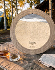Weathered Timber Brundage Mountain wooden cribbage board displayed on an outdoor cabin table beside whiskey glasses.
