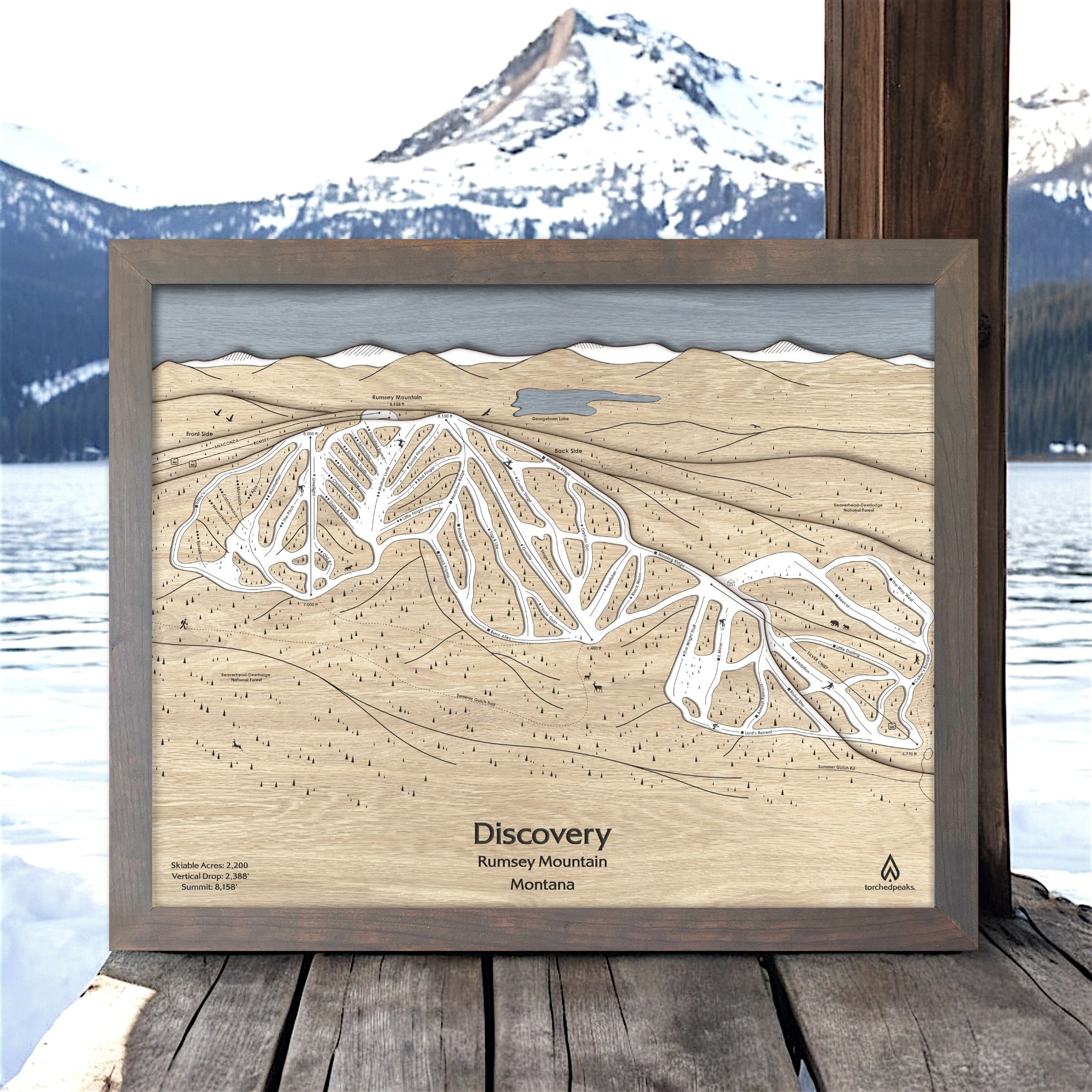 Wooden ski map of Discovery Ski Area with a lake, framed against a scenic background.