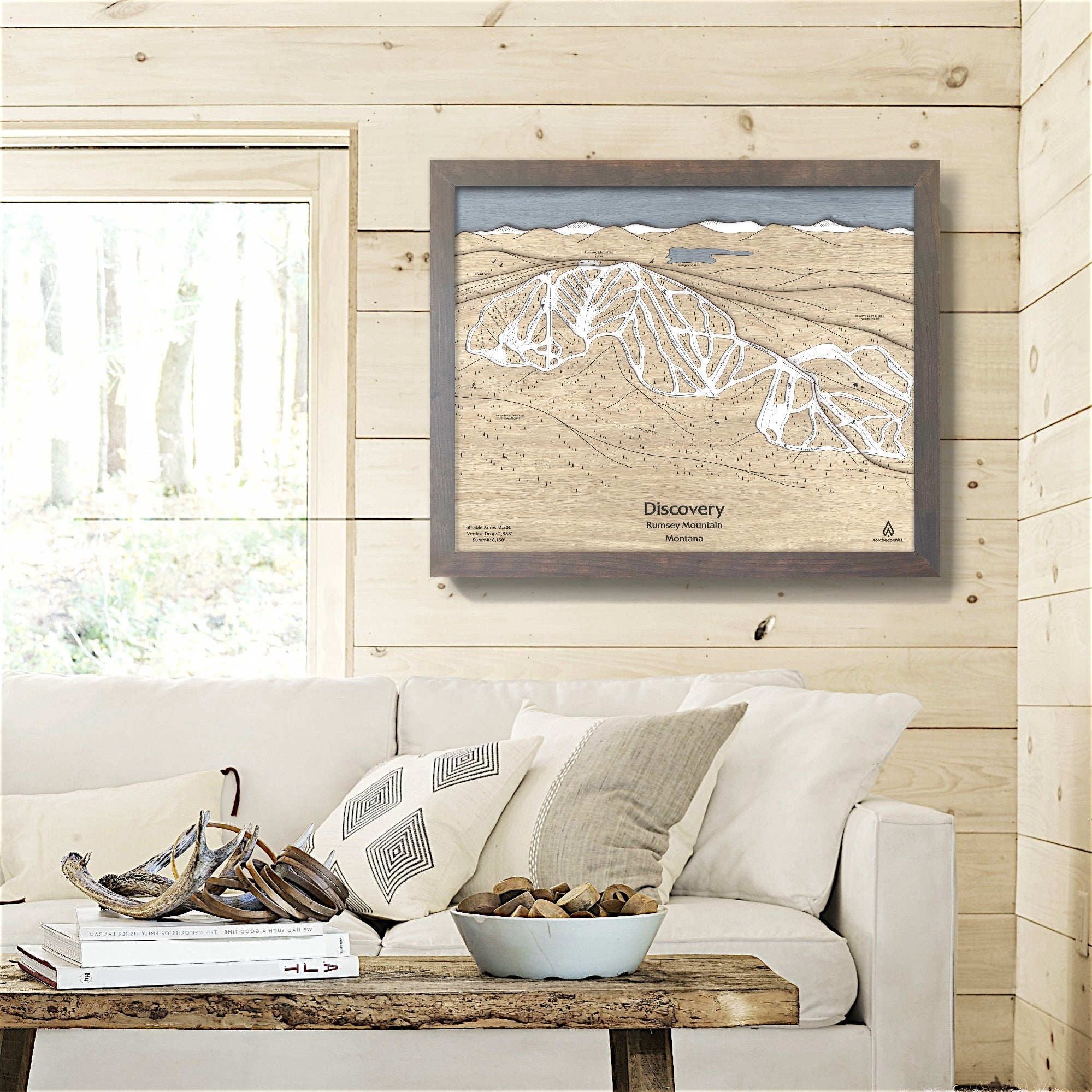 Framed wooden map of Discovery Ski Area  on a wall above a sofa in a living room inside a rustic ski cabin. 