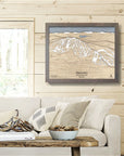 Framed wooden map of Discovery Ski Area  on a wall above a sofa in a living room inside a rustic ski cabin. 