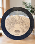 Handcrafted Heavenly Ski Trail Map Cribbage Board with a black walnut cribbage track, featuring an engraved wooden map of Heavenly Ski Resort, displayed on a mountain-inspired tabletop beside a coffee mug and evergreen arrangement.