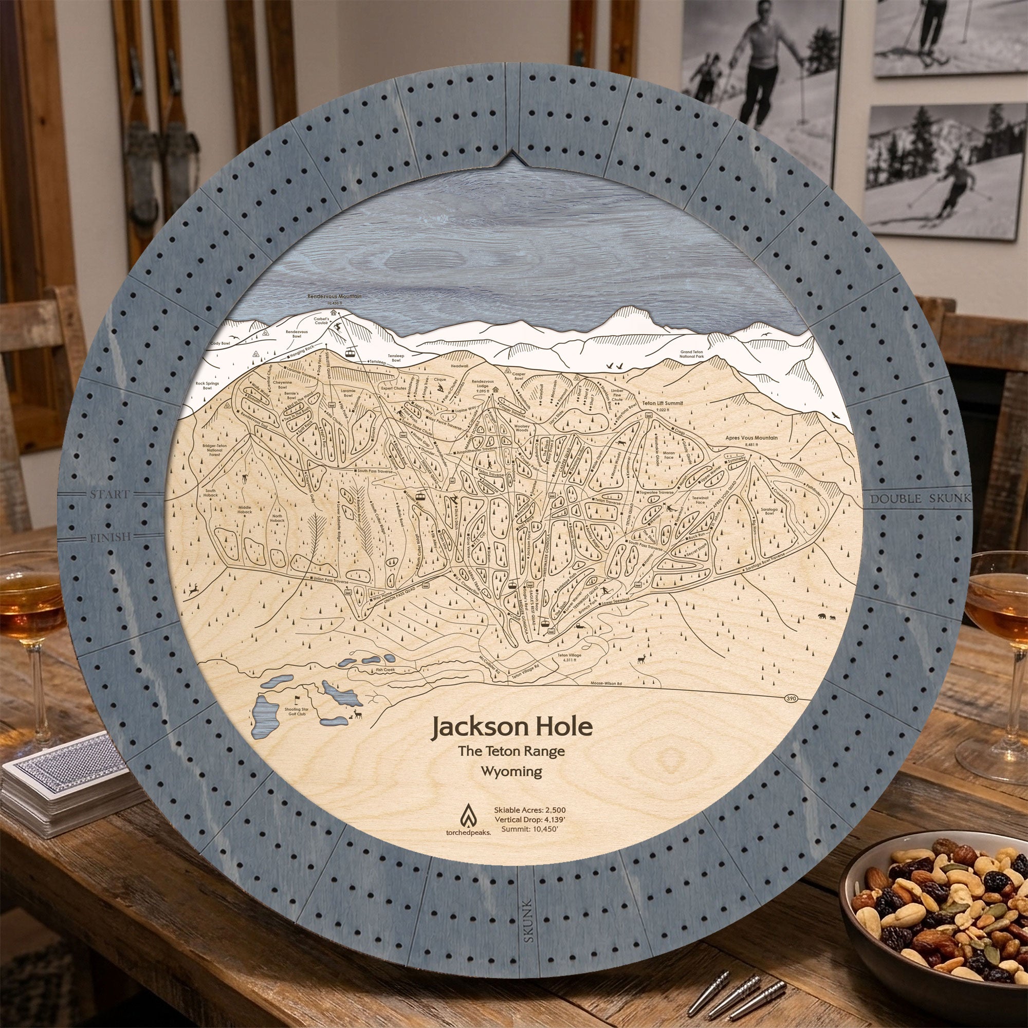 Graphite Grey Jackson Hole ski map cribbage board staged on a cabin table with playing cards and après-ski snacks.
