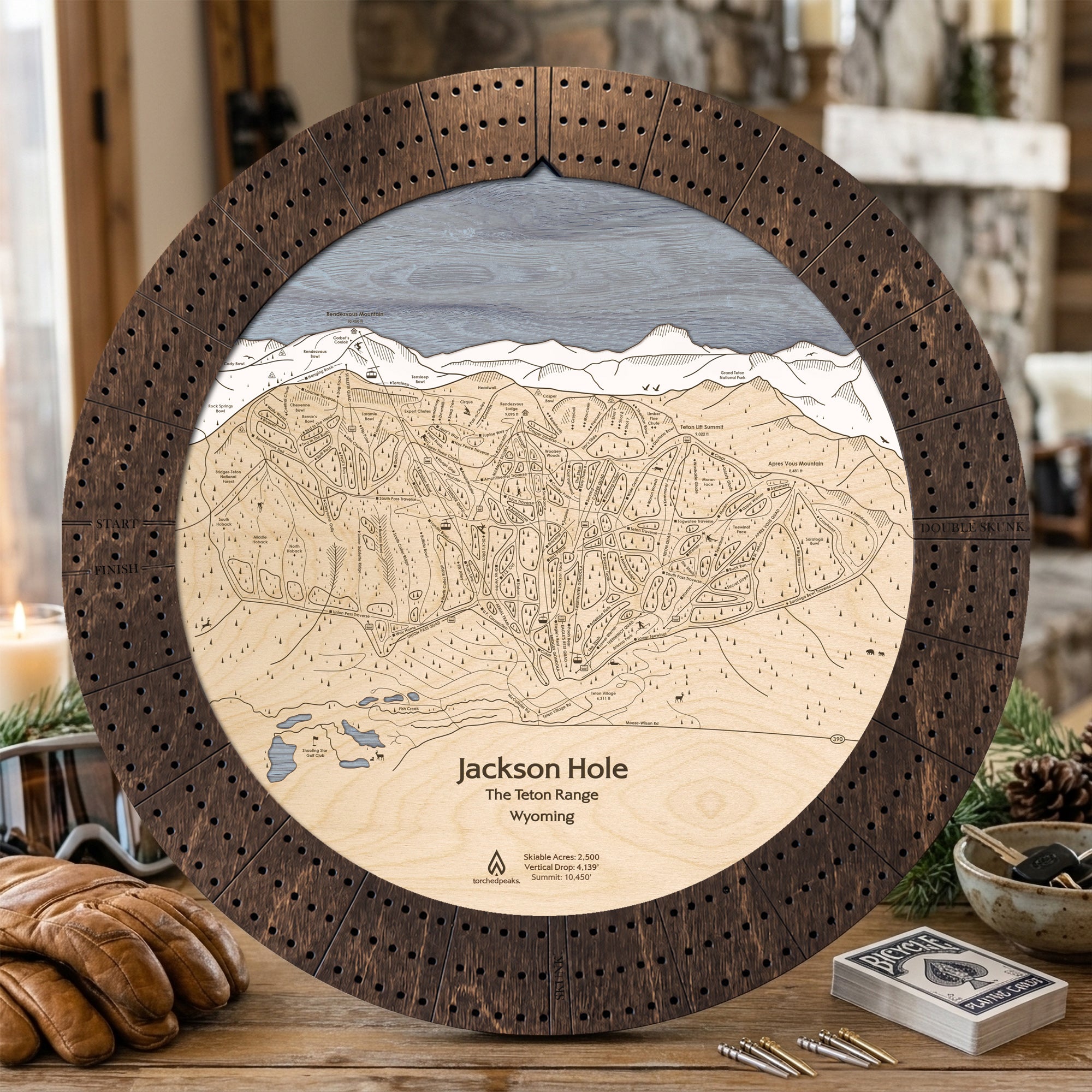 Rustic Mocha Jackson Hole ski trail map cribbage board displayed with playing cards in a mountain lodge.