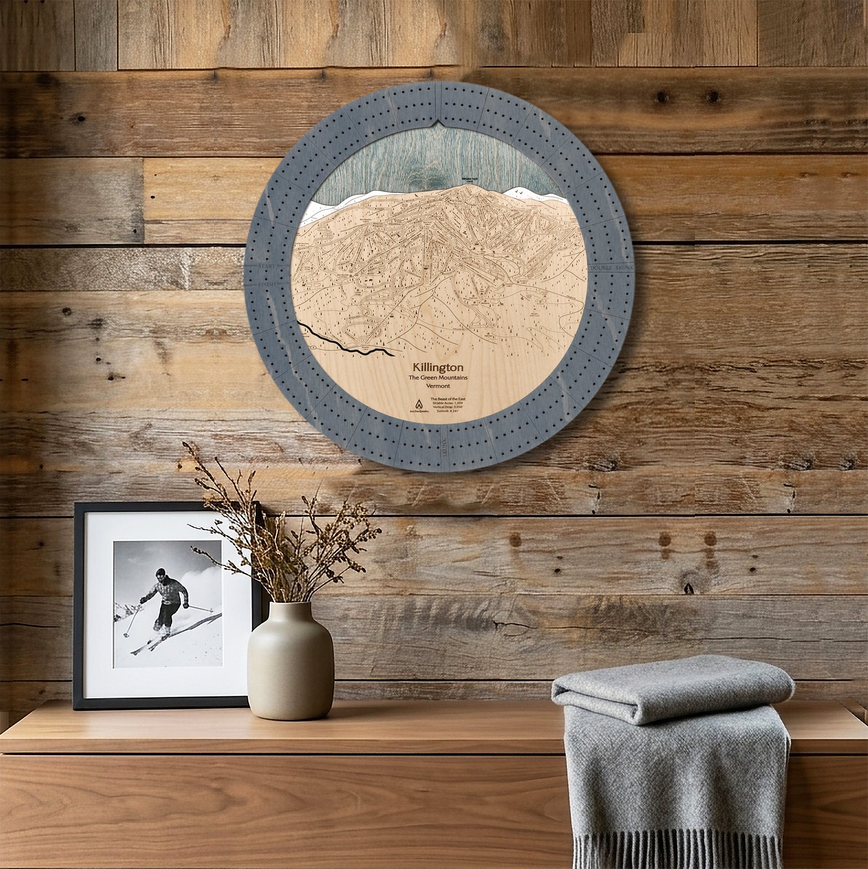 Killington ski trail map cribbage board displayed as round wall art above a rustic wood console inside a cozy ski cabin. 