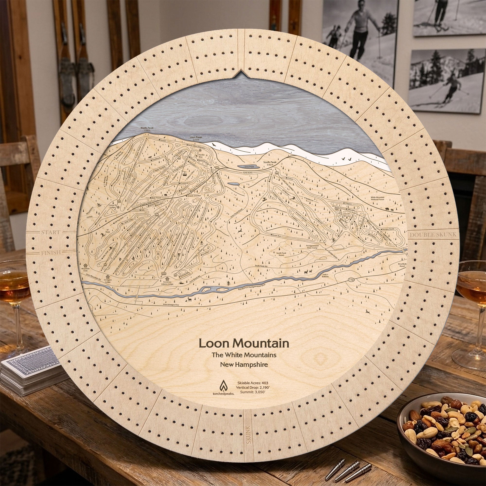 Birch Loon Mountain ski trail map cribbage board displayed on a wooden table beside playing cards and snacks. Example of apres ski board game. 
