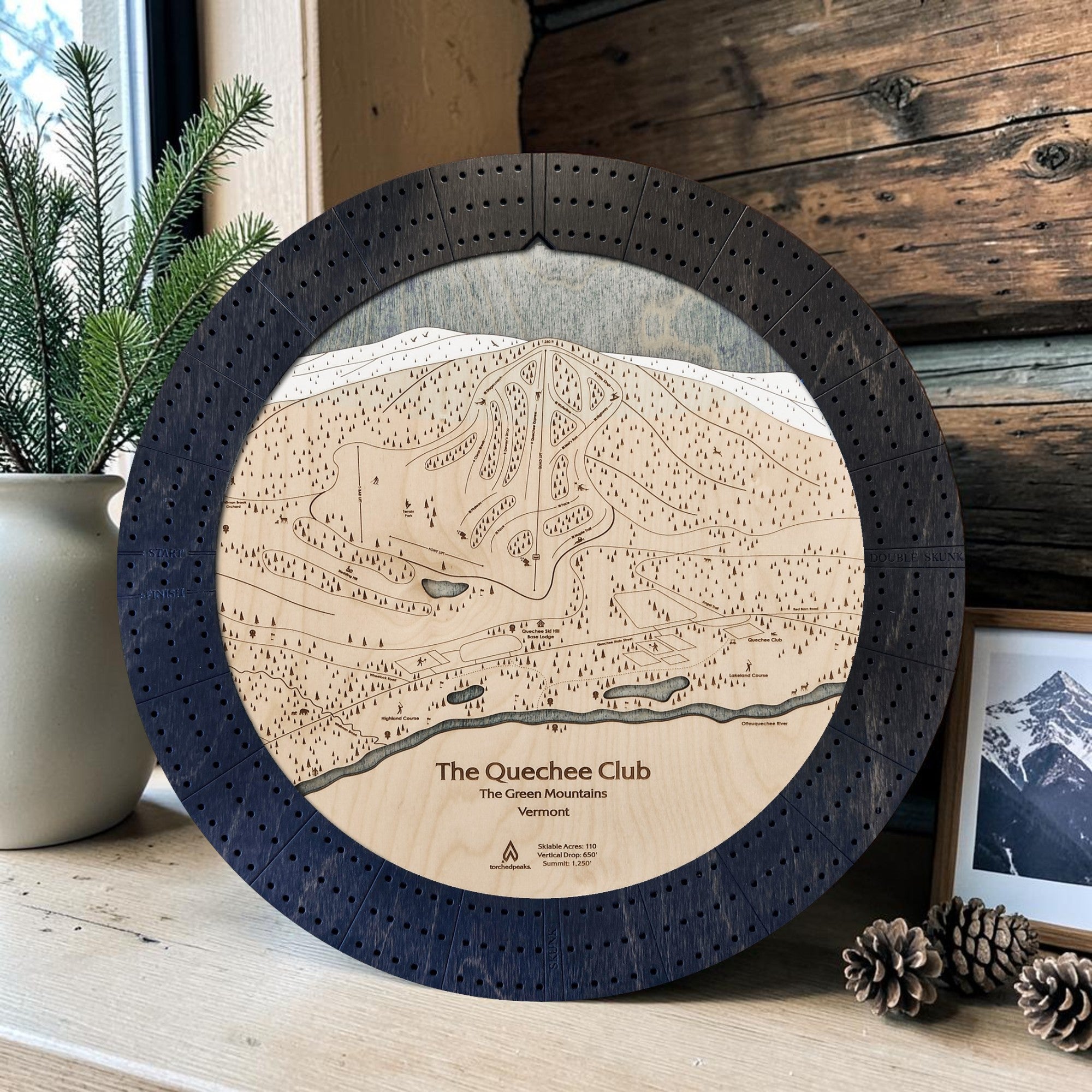 Matte Onyx Quechee Club ski map cribbage board displayed with pinecones and greenery as modern ski cabin décor.
