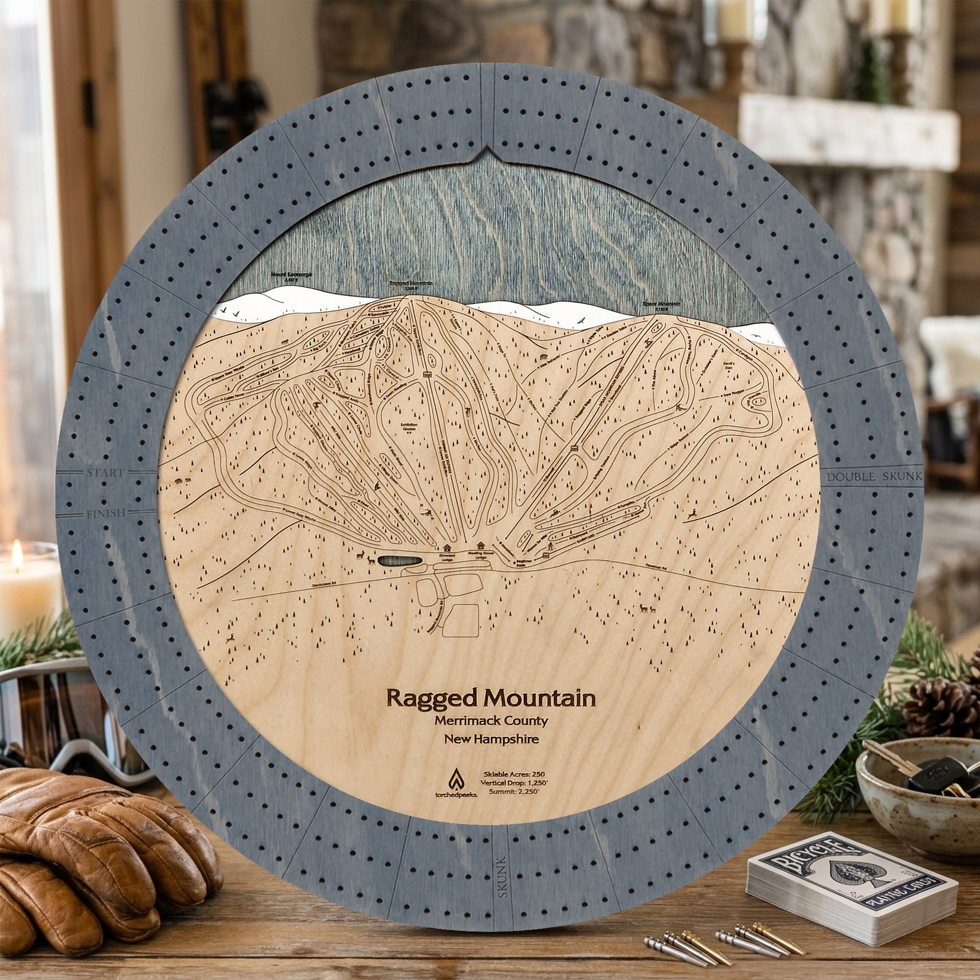 Ragged Mountain ski trail map cribbage board in Graphite Grey styled on a rustic table inside a ski cabin. 