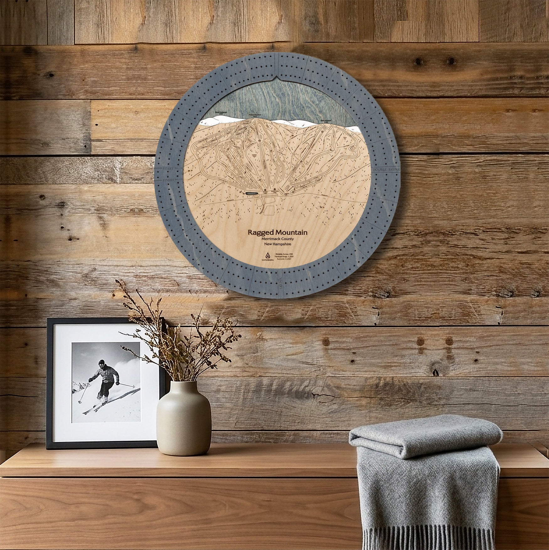 Ragged Mountain ski trail map cribbage board displayed as round wall art above a rustic wood console inside a cozy ski cabin. 