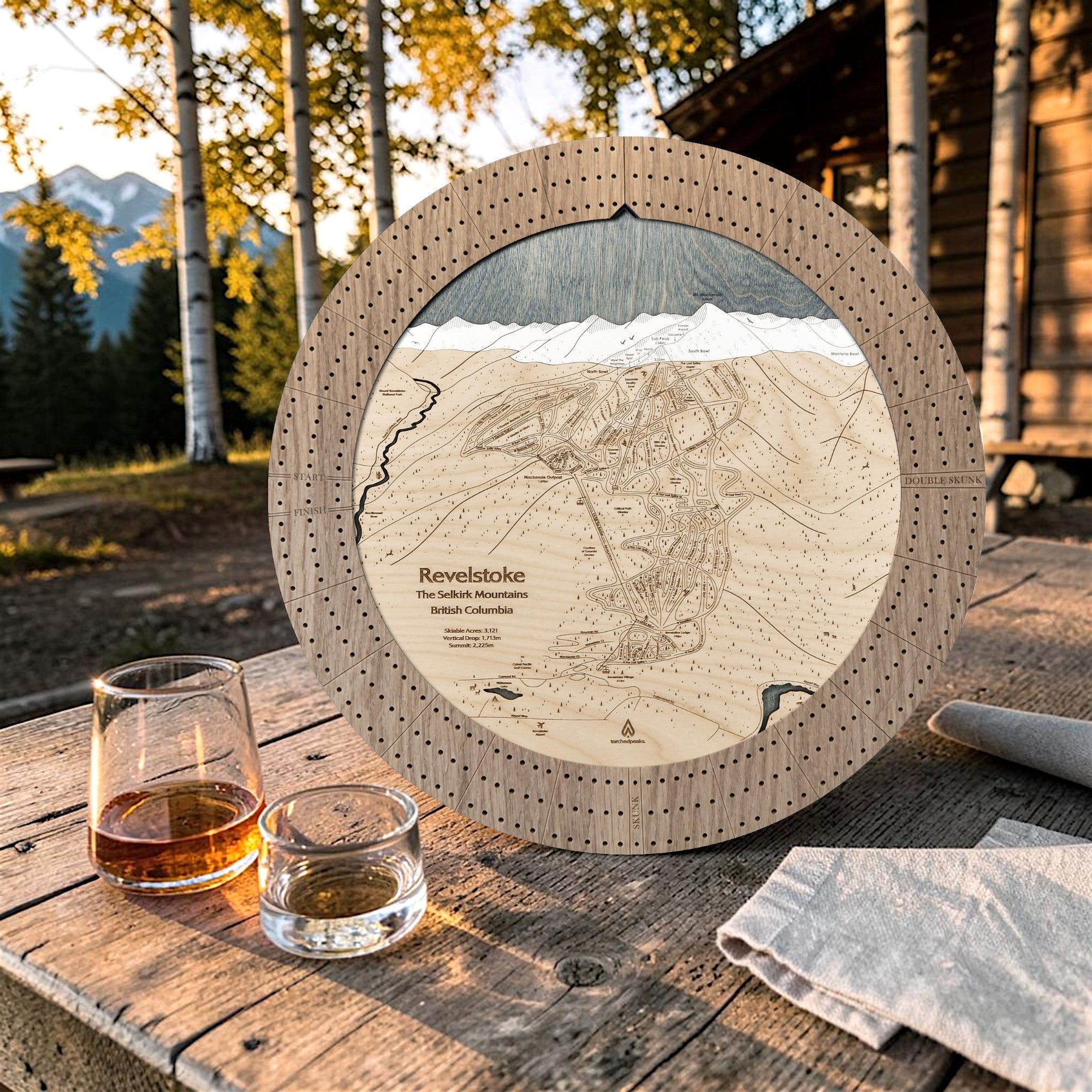 Weathered Timber Revelstoke ski map cribbage board outdoors with playing cards and whiskey glasses for après-ski game night.