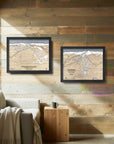 Two framed Torched Peaks Ski maps on a wooden wall with a couch and coffee table set in a rustic ski cabin. 