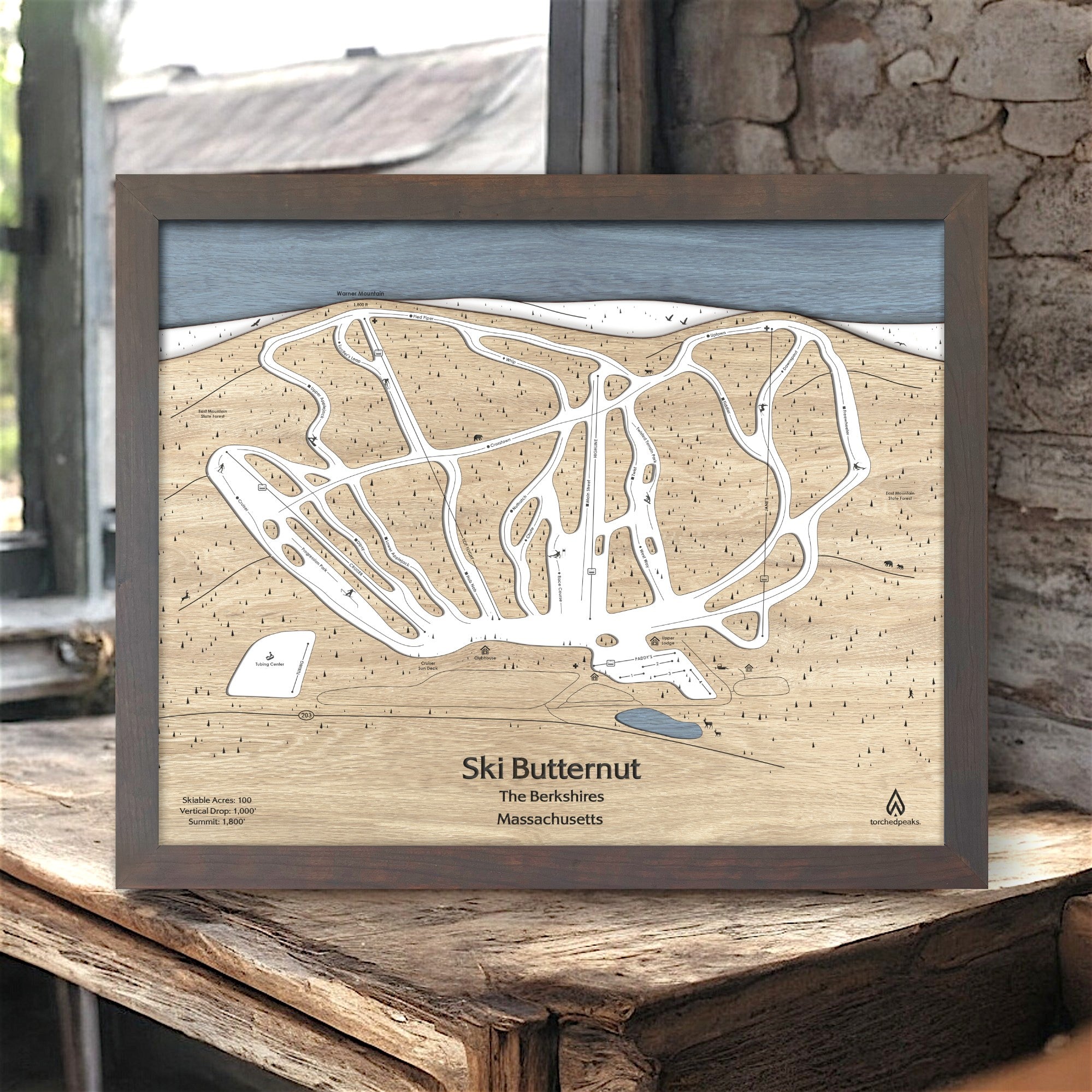 Framed wood wall map of Ski Butternut Ski Resort on a wooden surface inside a cozy ski cabin. 