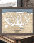 Framed wood wall map of Ski Butternut Ski Resort on a wooden surface inside a cozy ski cabin. 