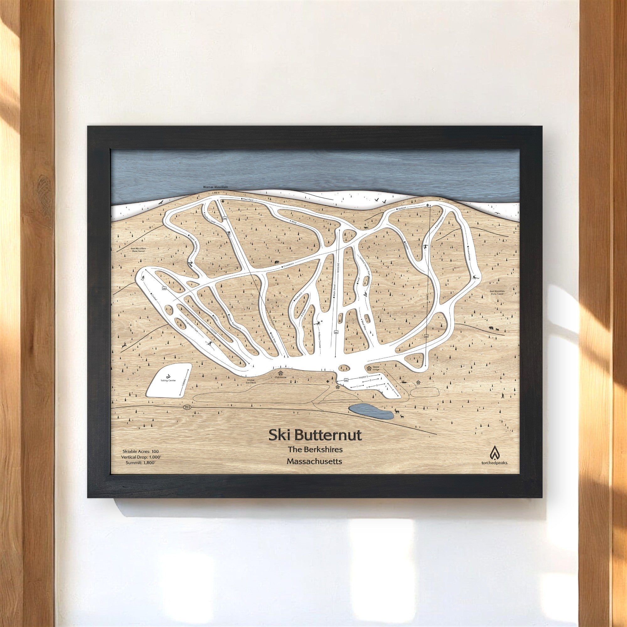 Framed wooden map of Ski Butternut Ski Resort on a white wall in a ski cabin. 