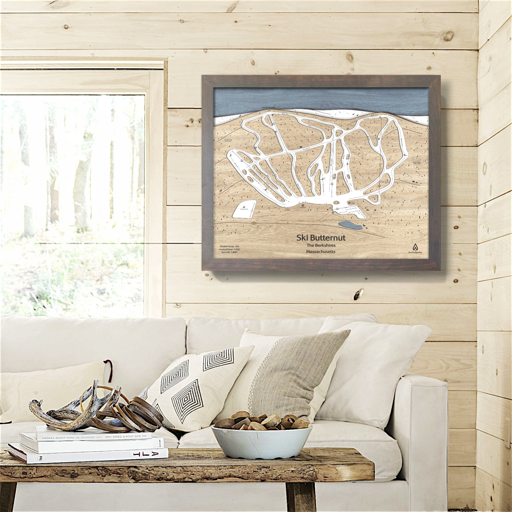 Framed wooden map of butternut ski resort on a wall above a sofa in ski house.