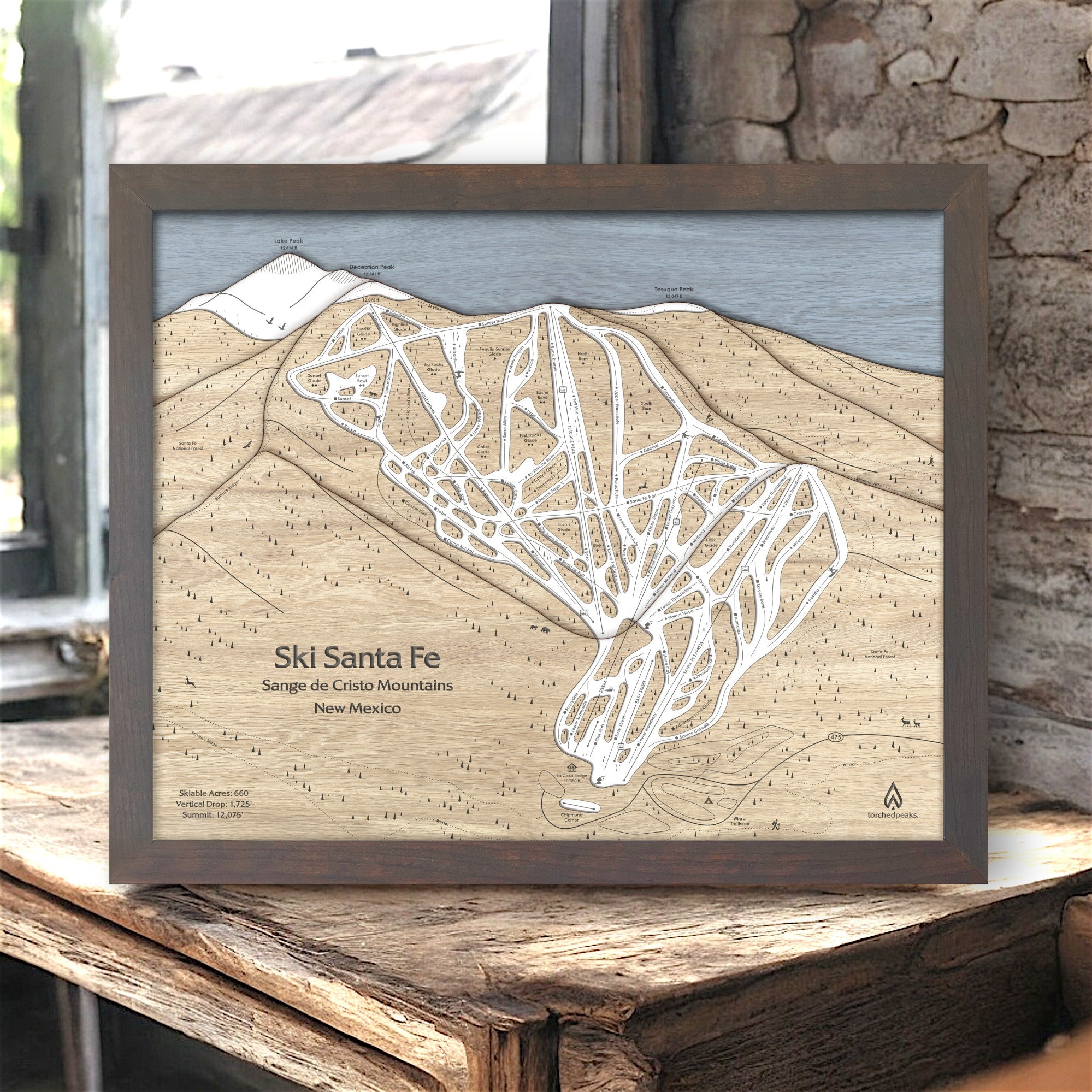 Framed 3d wood map of Ski Santa Fe in New Mexico on a wooden surface inside a rustic ski cabin. 