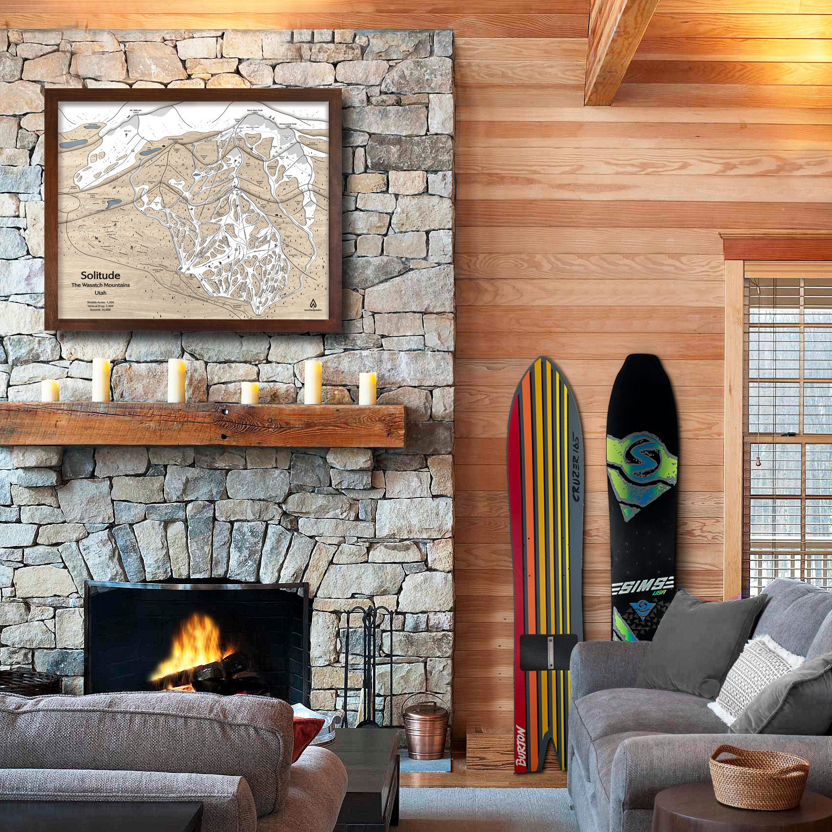 Living room with stone fireplace, large format solitude ski map, gray sofa, and two snowboards against a wooden wall.