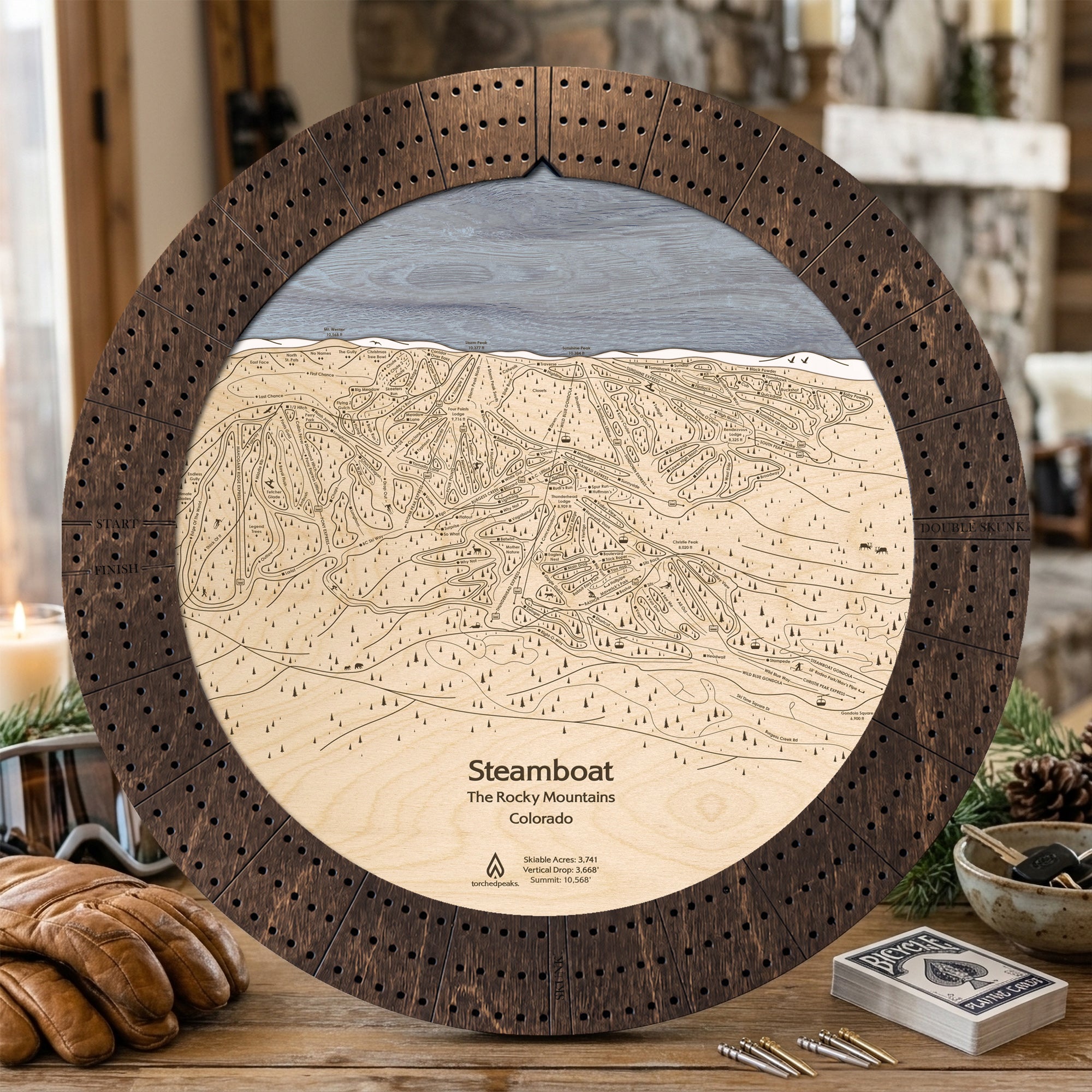 Rustic Mocha Steamboat ski map cribbage board staged with playing cards and après-ski snacks in a mountain lodge.