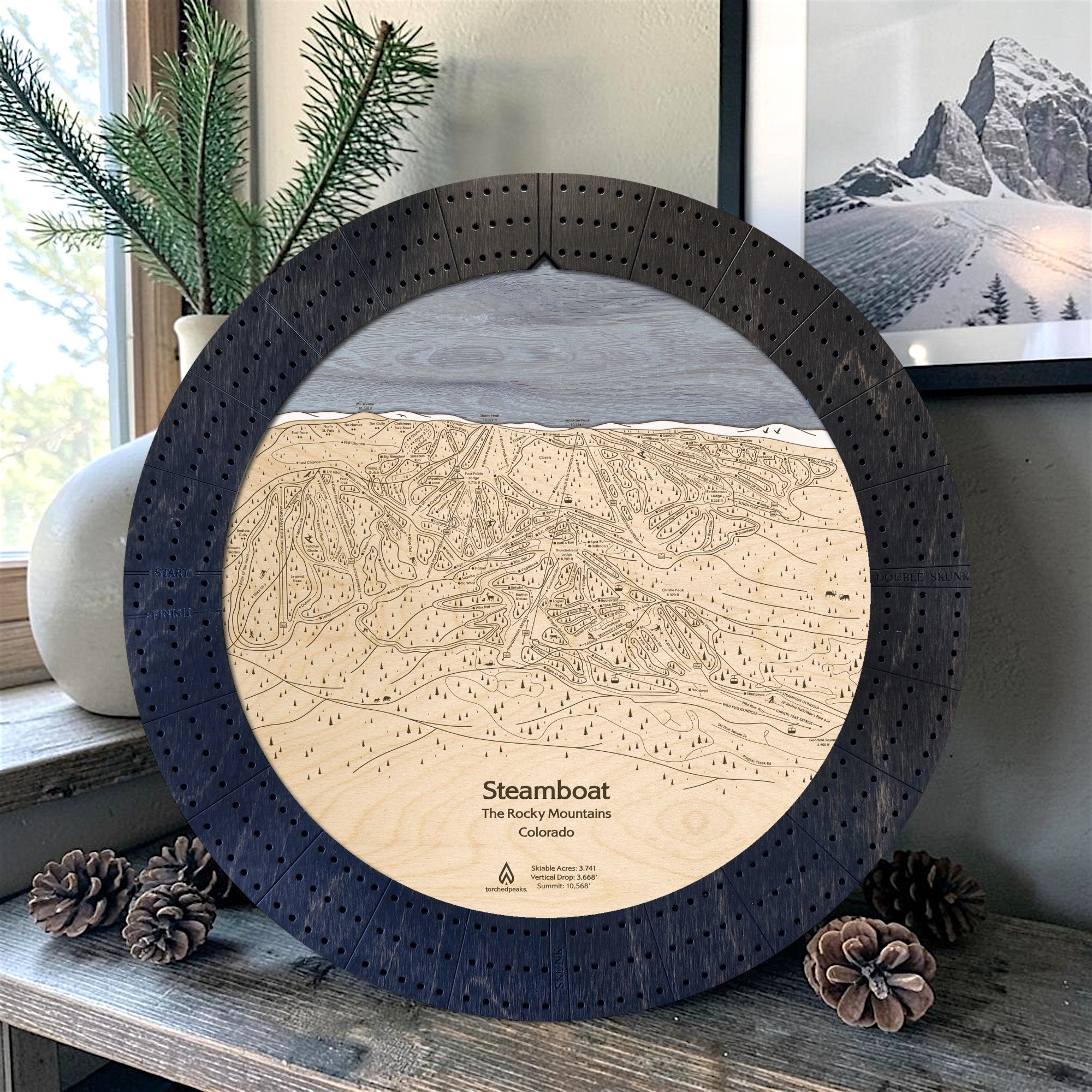 Matte Onyx Steamboat ski map cribbage board displayed with pinecones as modern ski cabin décor.