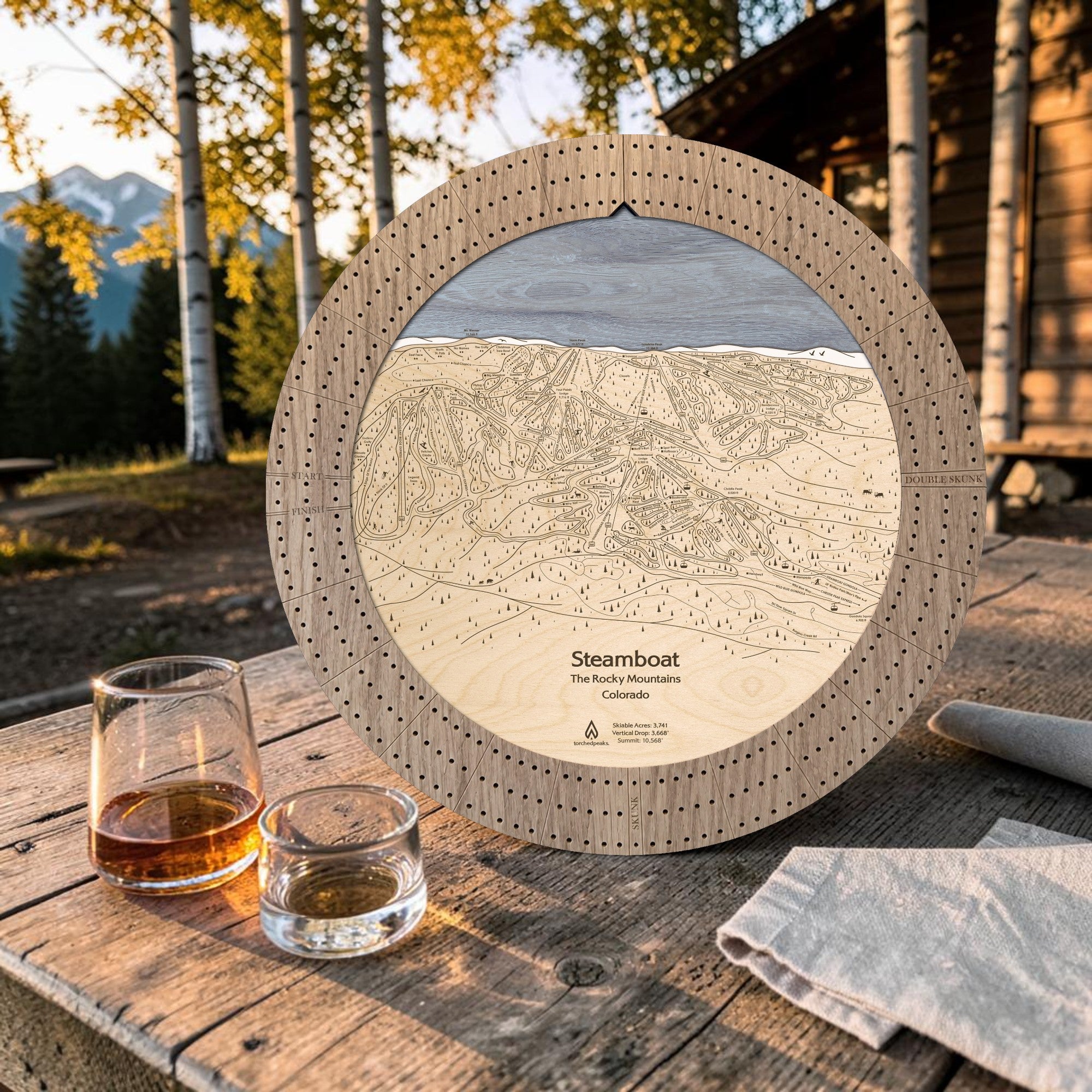Weathered wood Steamboat ski map cribbage board outdoors with whiskey glasses and cards for après-ski game night.