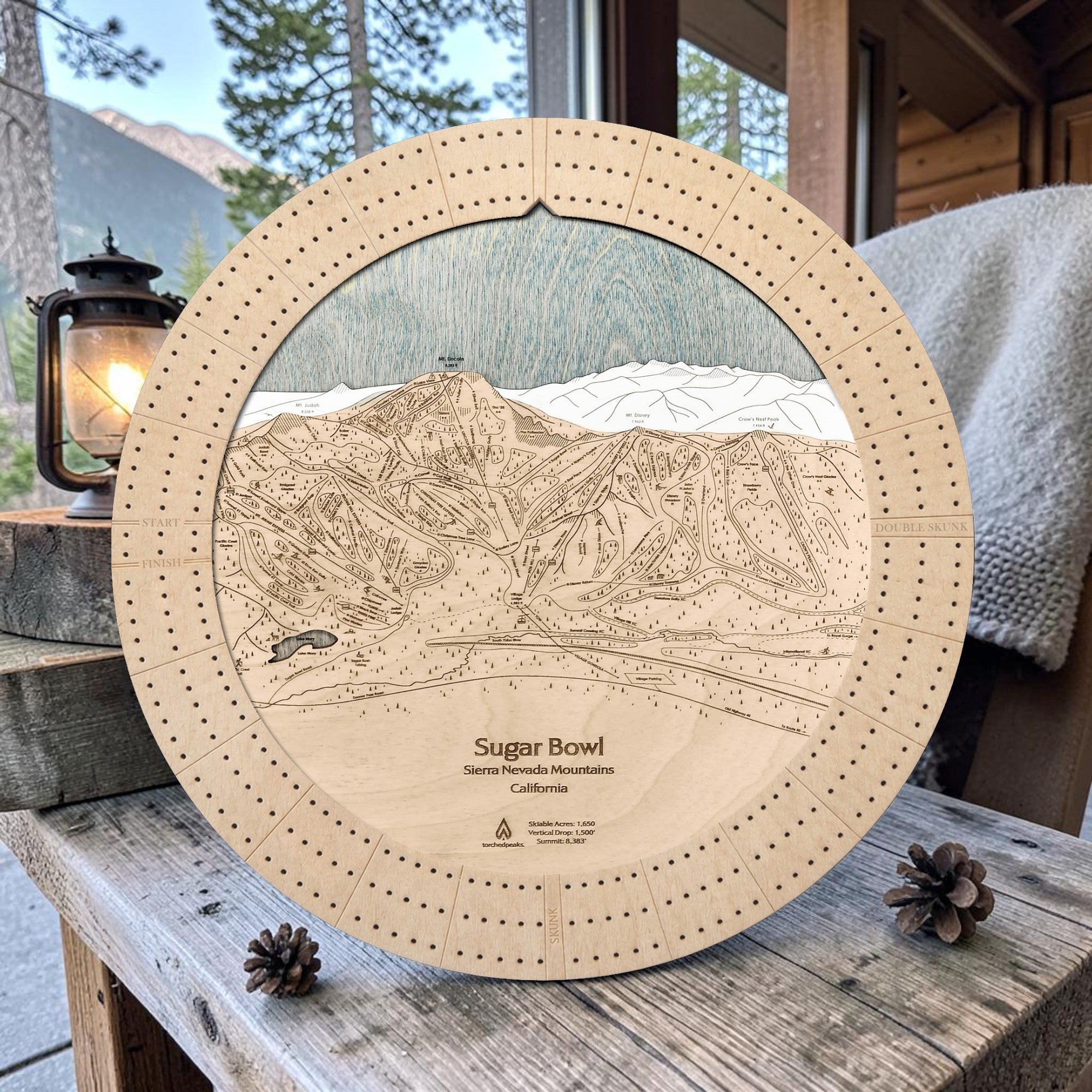 Sugar Bowl wooden ski trail map cribbage board in Birch displayed on a rustic cabin bench.