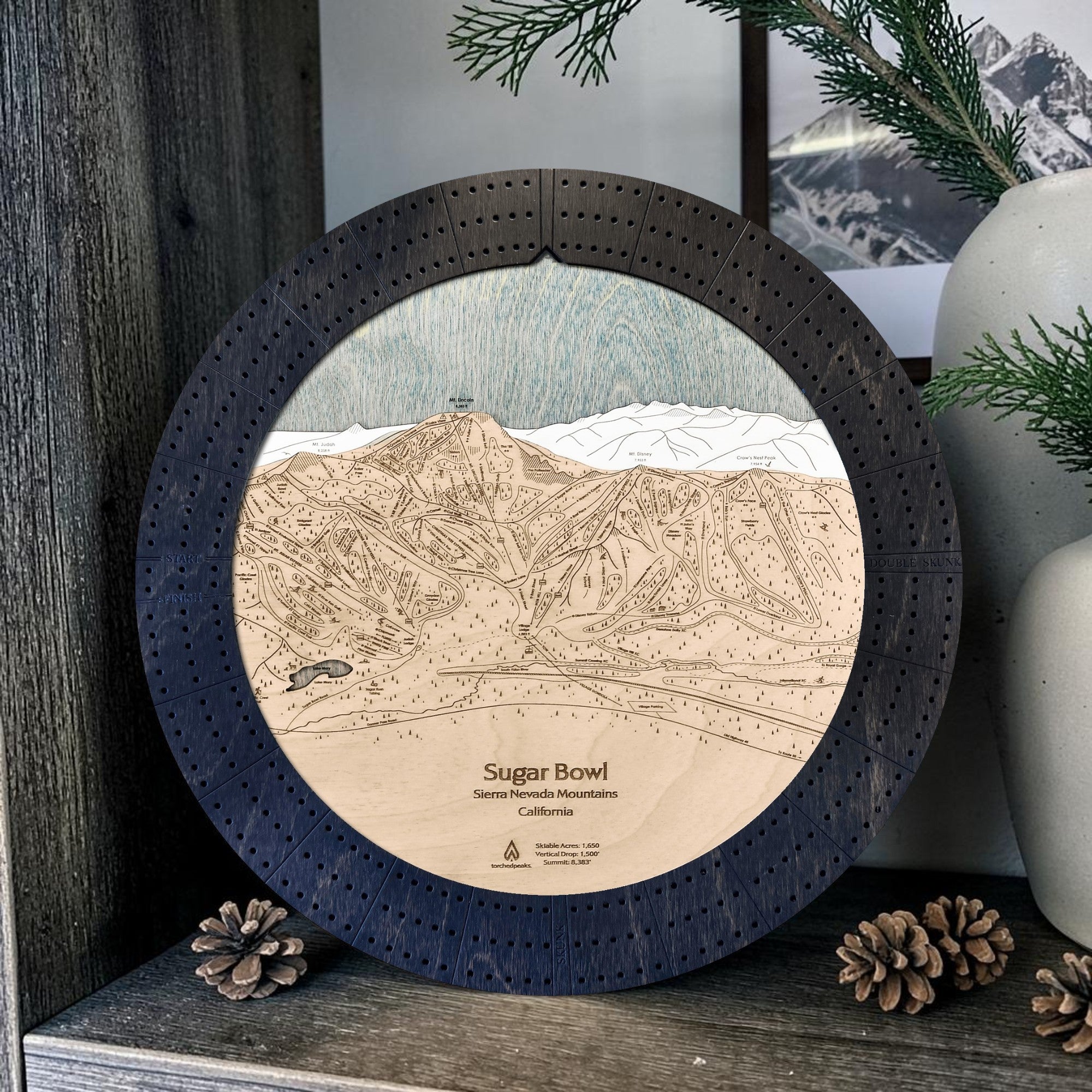 Sugar Bowl wooden cribbage board in Matte Onyx displayed with mountain décor and pinecones.