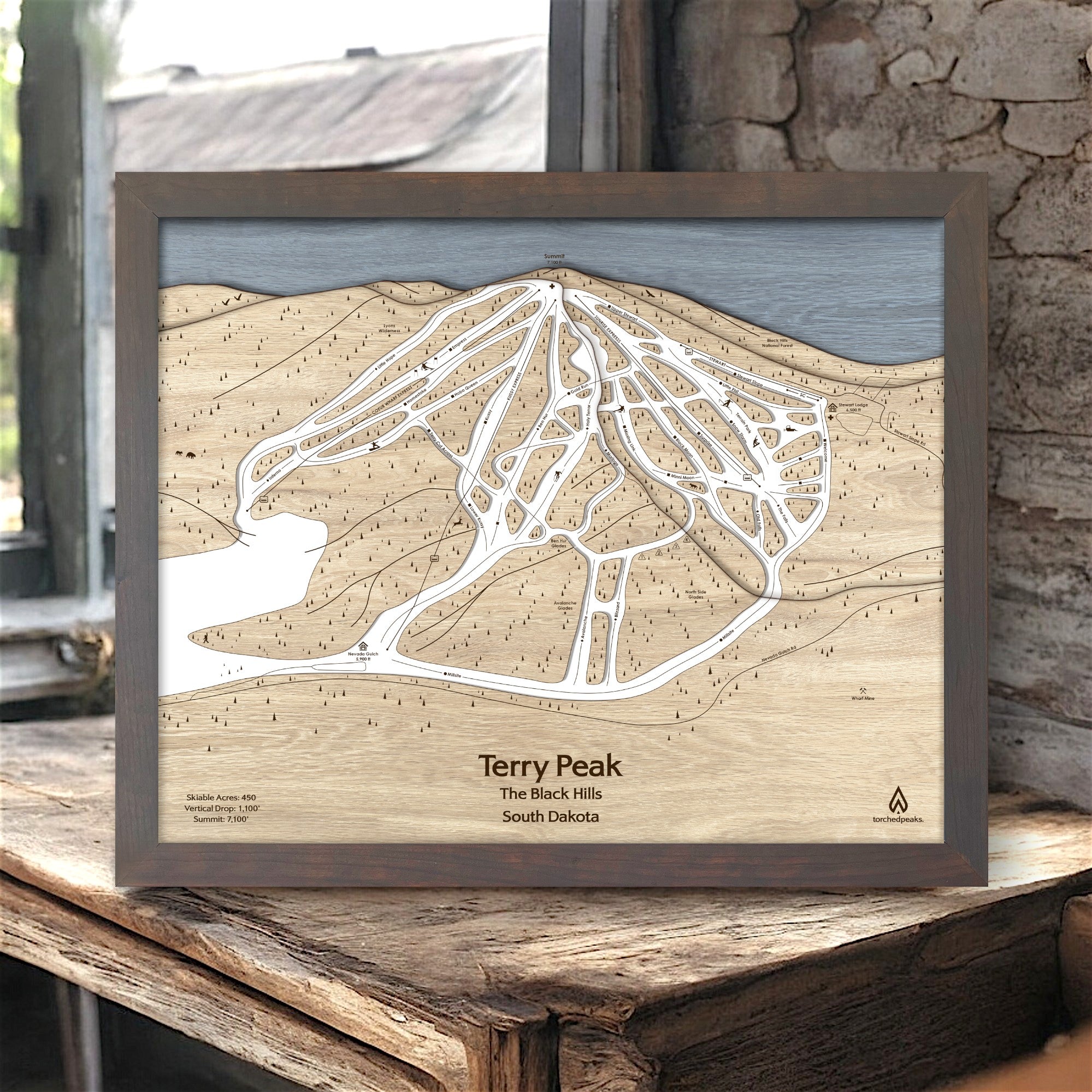 Framed laser-cut map of Terry Peak ski trails in South Dakota on a wooden surface inside a rustic ski cabin. 