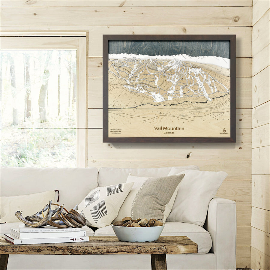 Framed 3D landscape print of Vail Mountain on a wooden wall above a sofa.