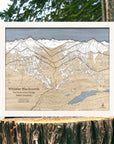Whistler Blackcomb 3D wood ski map with an Arctic White frame displayed outdoors on a snowy forest stump.