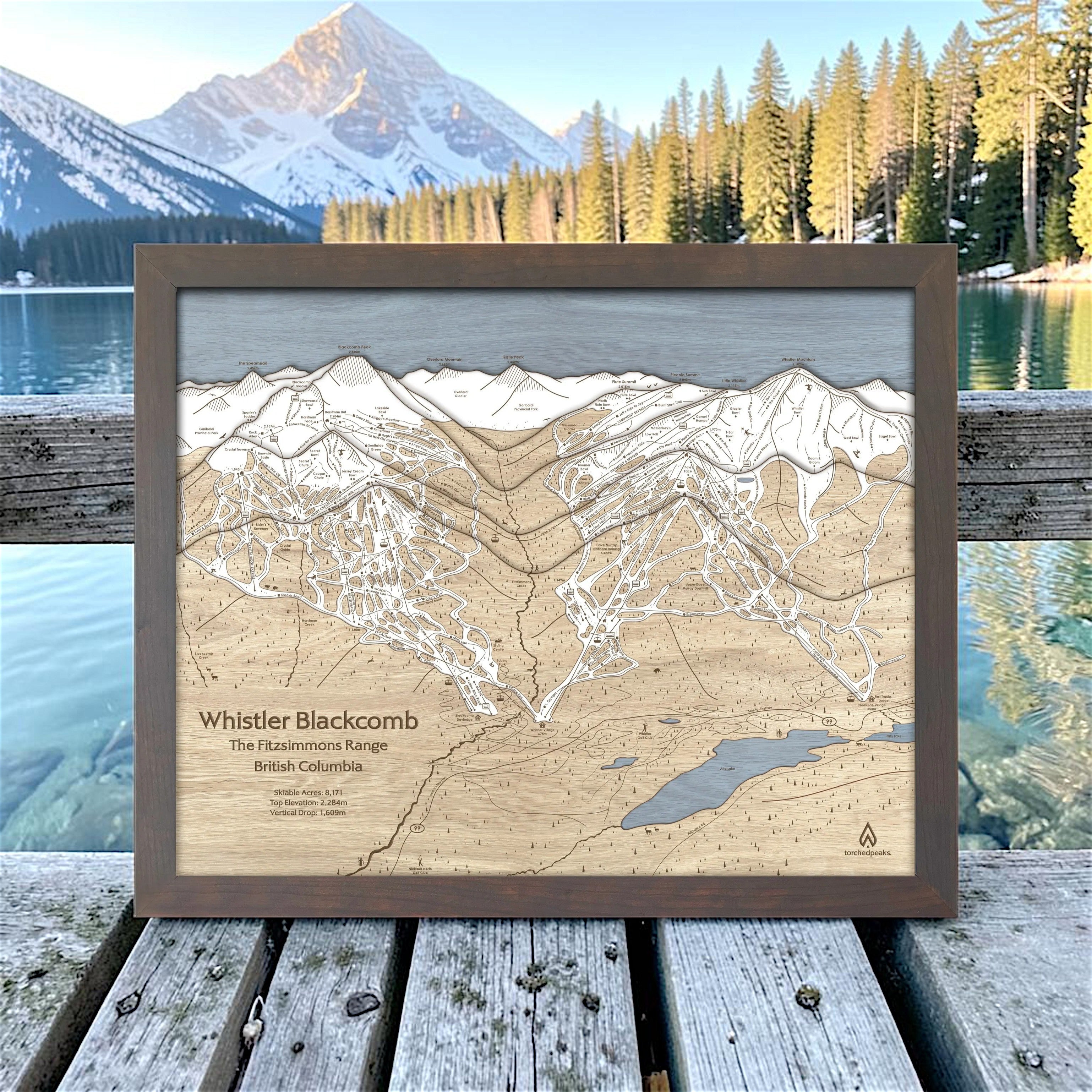 Graphite-framed Whistler Blackcomb wood ski map displayed on a deck overlooking an alpine lake and mountains