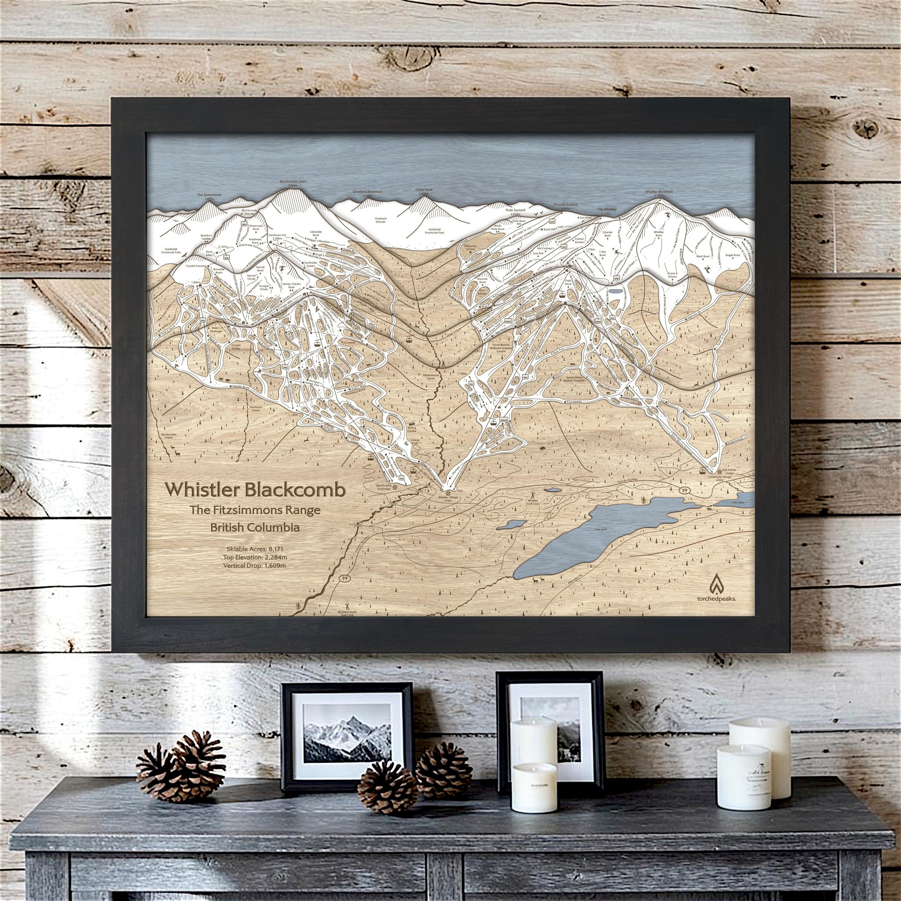 Whistler Blackcomb 3D wood ski map with a Matte Onyx frame on a whitewashed cabin wall above a rustic console.