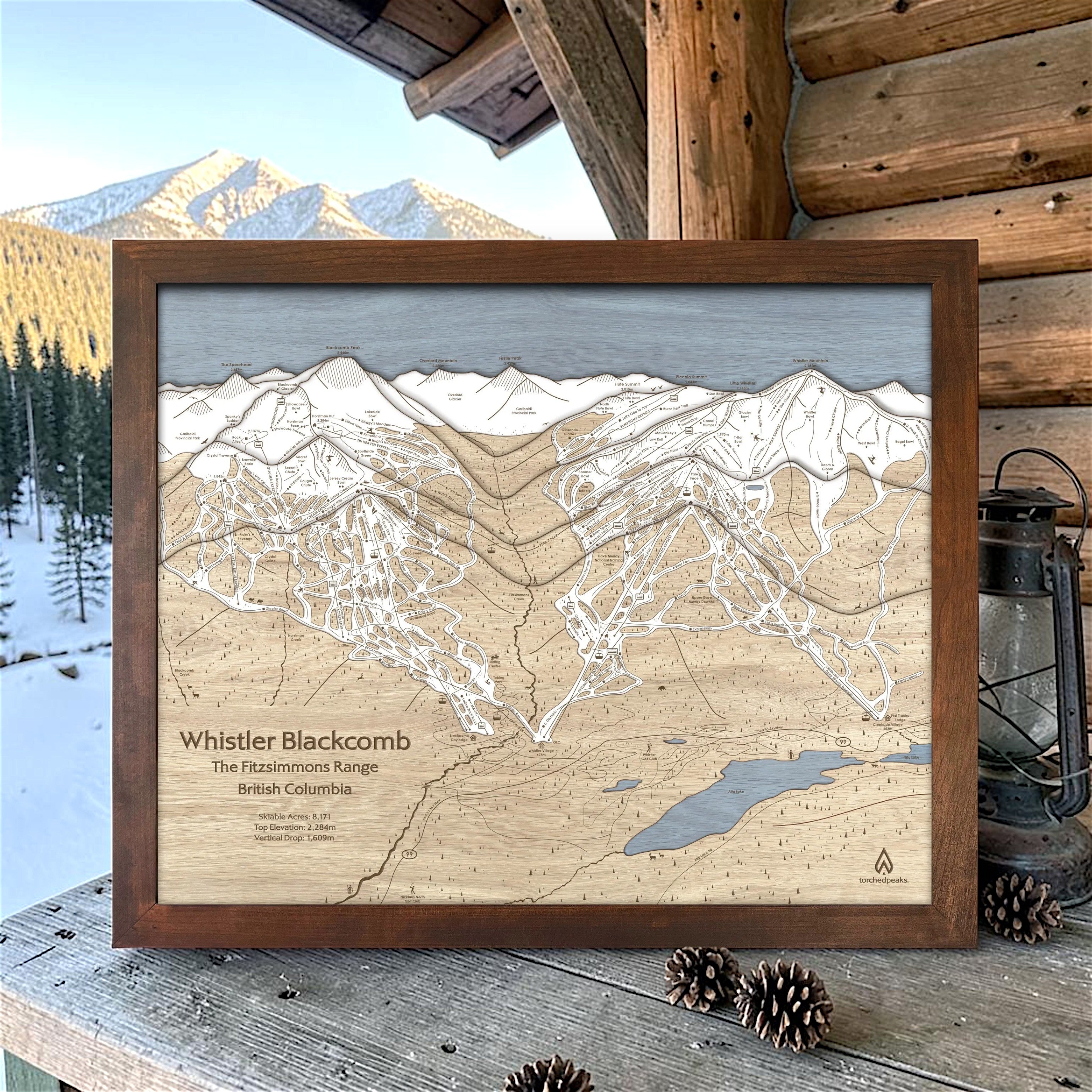 Rustic Mocha-framed Whistler Blackcomb ski map displayed on a cabin deck with snowy mountains in the distance.